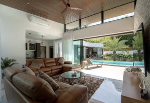 Ein modernes Wohnzimmer mit einer Ledersofa, einem Glastisch und Blick auf einen Swimmingpool sowie eine Sitzgelegenheit im Freien.