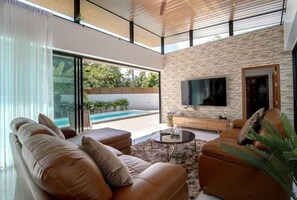 Ein modernes Wohnzimmer mit Pool, Ledersofas, Fernseher und Steinwand.