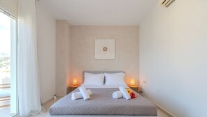 A neatly made bed with white linens and a gray blanket, two bedside lamps, and a framed picture on the wall. - Villa Nero -
A beautiful 2-bedroom villa with Mini Pool, 5 min from the beach! (PLAKIAS)