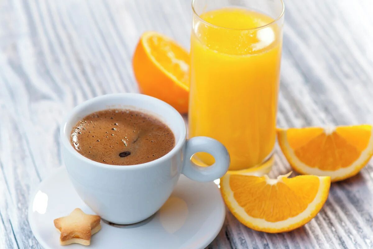 A cup of coffee, a glass of orange juice, and orange slices on a white plate.