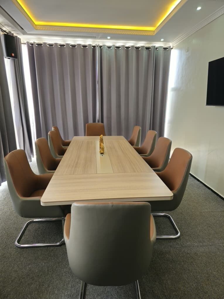 A conference room with a long table and modern chairs, a flat-screen TV, and a ceiling light fixture.
