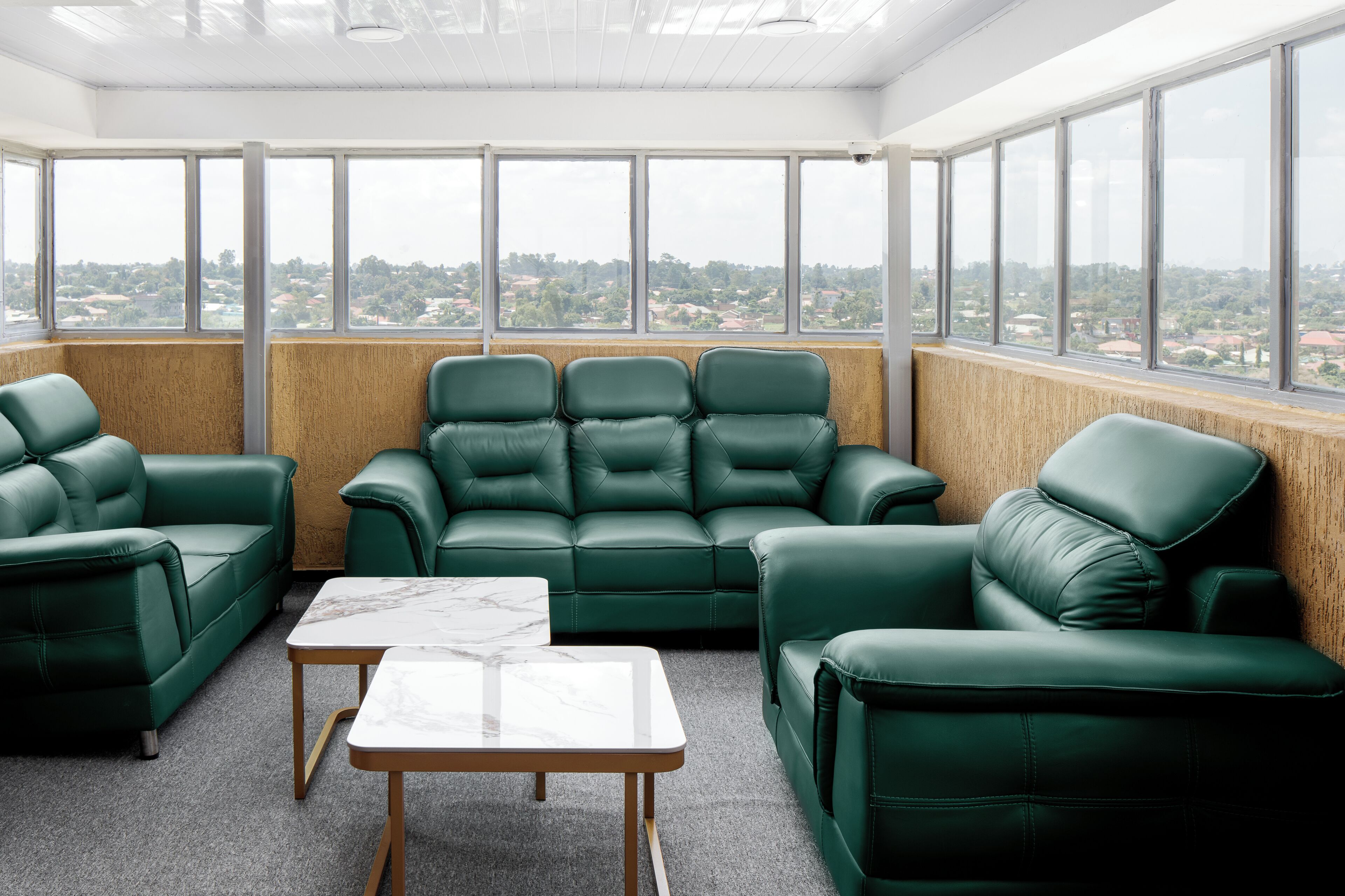 Habitación con sofá de cuero verde, una mesa con cubierta de mármol y ventanas amplias que ofrecen vistas a la ciudad.