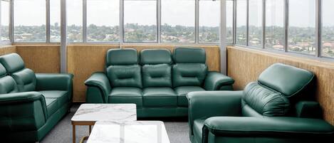 A room with a green leather sofa set, a marble-topped table, and large windows offering a view of a cityscape.