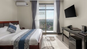 Une chambre d’hôtel équipée d’un lit, d’un bureau, d’une télévision à écran plat et offrant une vue sur l’extérieur grâce à une grande fenêtre.
