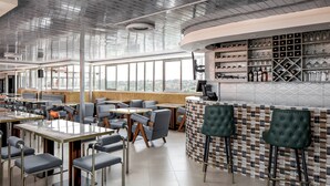 Un restaurant moderne avec de hauts plafonds, de grandes fenêtres et un bar doté d’étagères remplies de verres et de bouteilles.