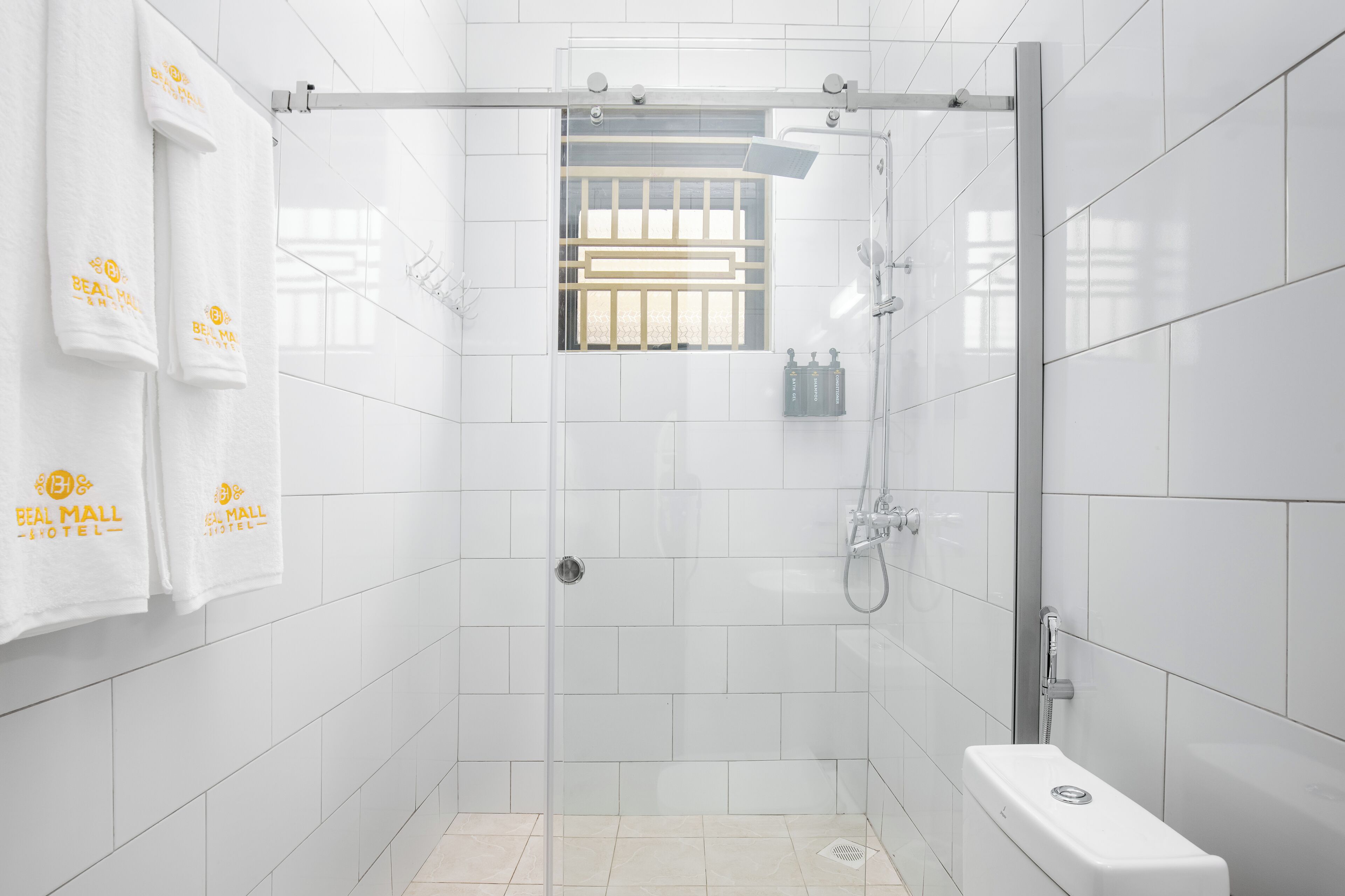 A modern bathroom with white tiles, a glass-enclosed shower, a toilet, and two towels hanging on the wall.