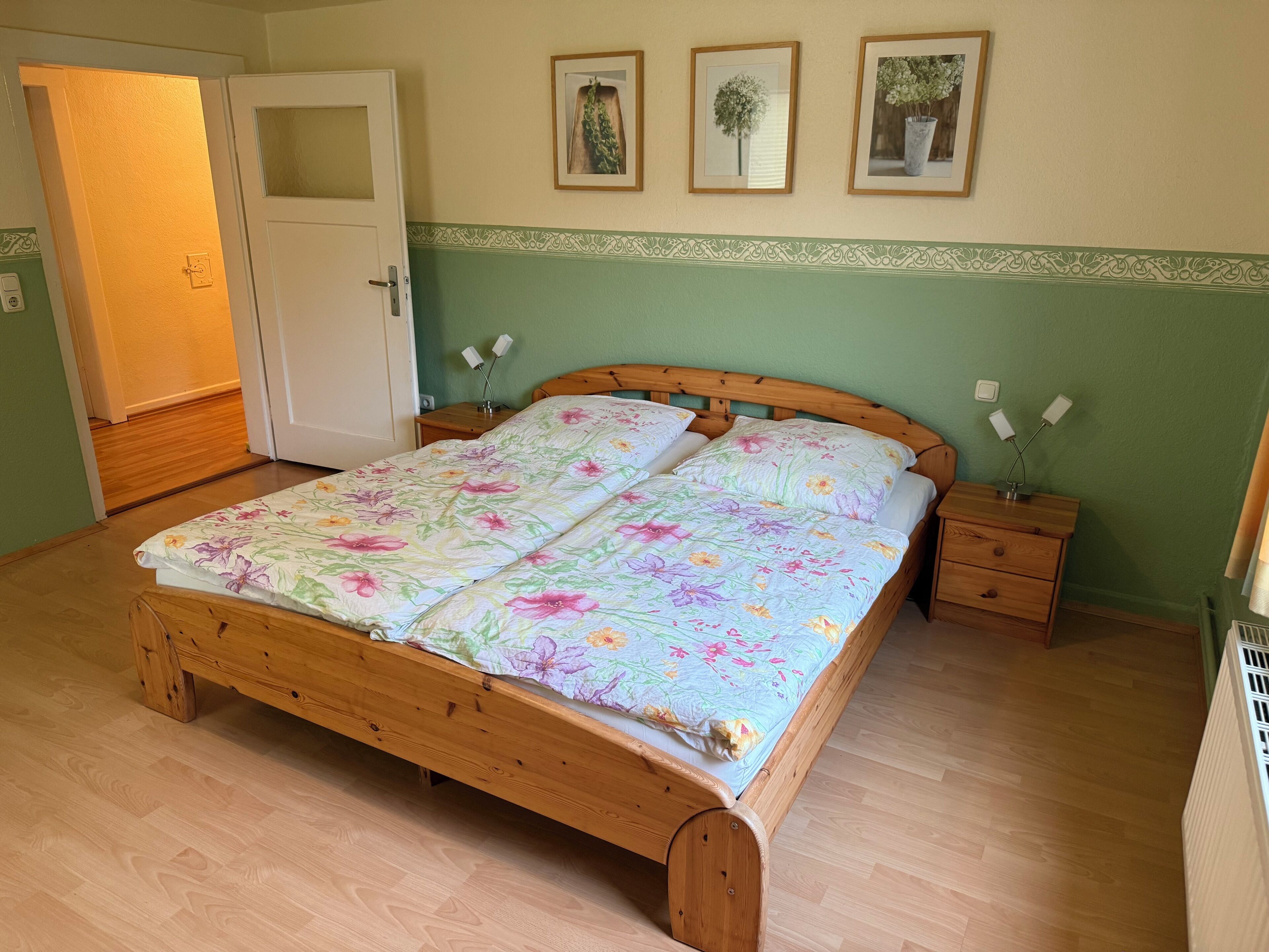 A bedroom with a wooden bed, floral bedding, a green accent wall, and three framed pictures.