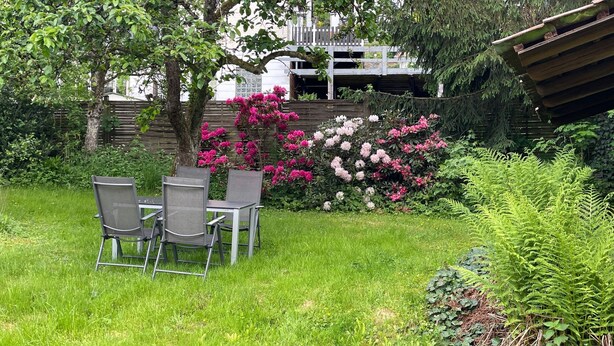 Un jardin agrémenté d’une table et de chaises, entouré d’une végétation luxuriante et de plantes en fleurs.