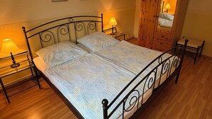 Un lit avec un cadre en métal, deux tables de chevet avec des lampes, un plancher en bois, une armoire en bois et deux tableaux encadrés accrochés au mur.