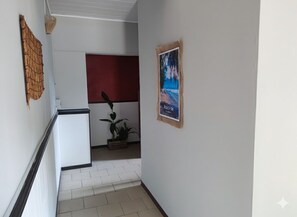 Een gang met een witte muur, een rode panelenwand, een poster en een plant.