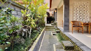 A narrow pathway flanked by lush greenery and stone walls, leading to a seating area with a wooden table and chairs. - Anugrah Twin Ubud (Ubud)
