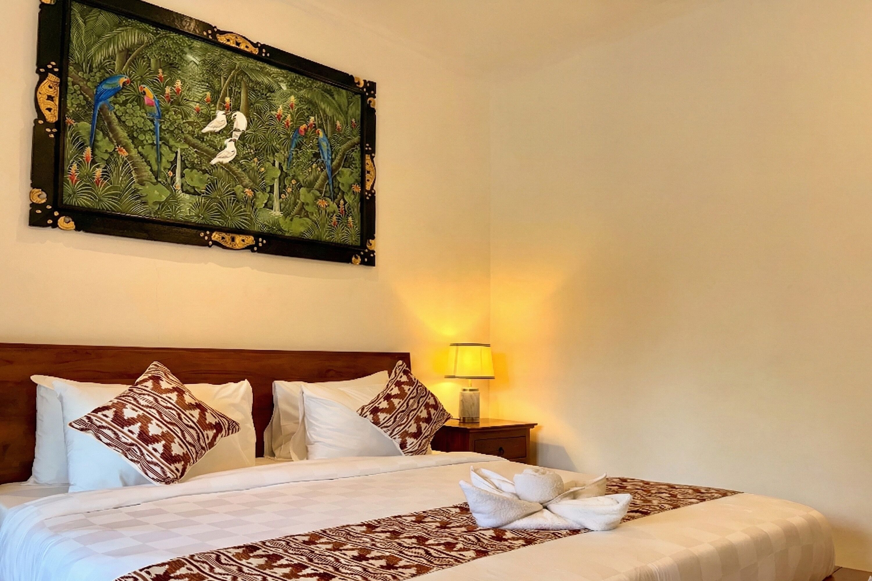 Une chambre d’hôtel avec un grand lit, des oreillers à motifs, une table de chevet avec une lampe et un tableau encadré au-dessus du lit.