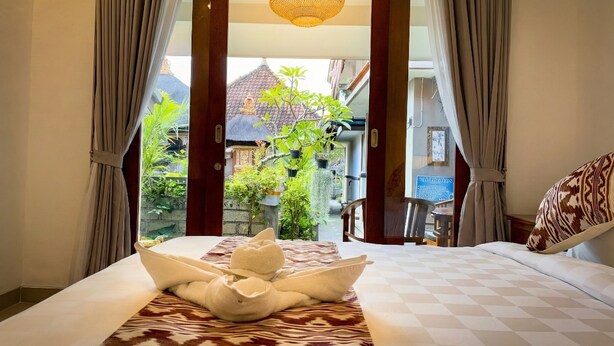 A hotel room with a bed, a view of the garden, and a hanging light fixture. - Anugrah Twin Ubud (Ubud)