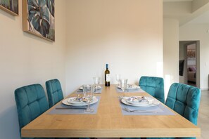 Een eettafel gedekt met borden, glazen en bestek, met aan weerszijden teal bekleden stoelen, en een fles wijn op de tafel.