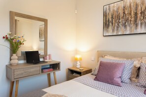 Een slaapkamer met een bed, een bureau met een laptop, een nachtkastje met een lamp en een aan de muur hangend schilderij.