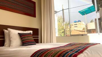 Una camera d'albergo con un letto grande, vista all'esterno tramite una finestra e un arcobaleno nel cielo.