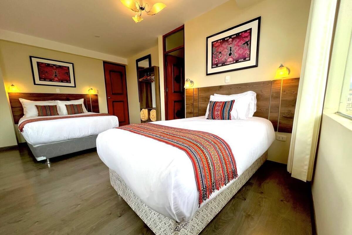 A hotel room with two beds, wooden flooring, and artwork on the walls.