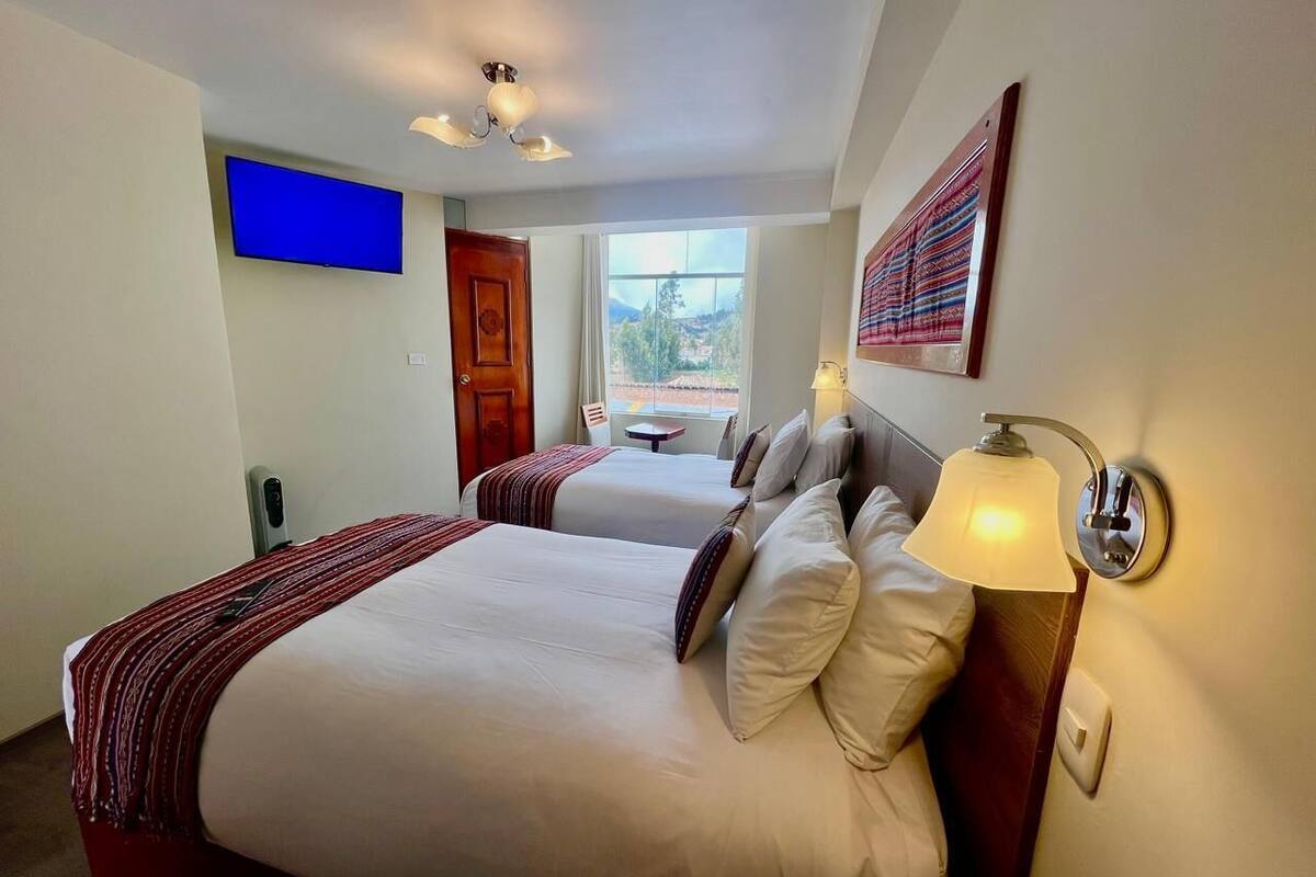 A hotel room with two beds, a TV, a window with a view, and a lamp.