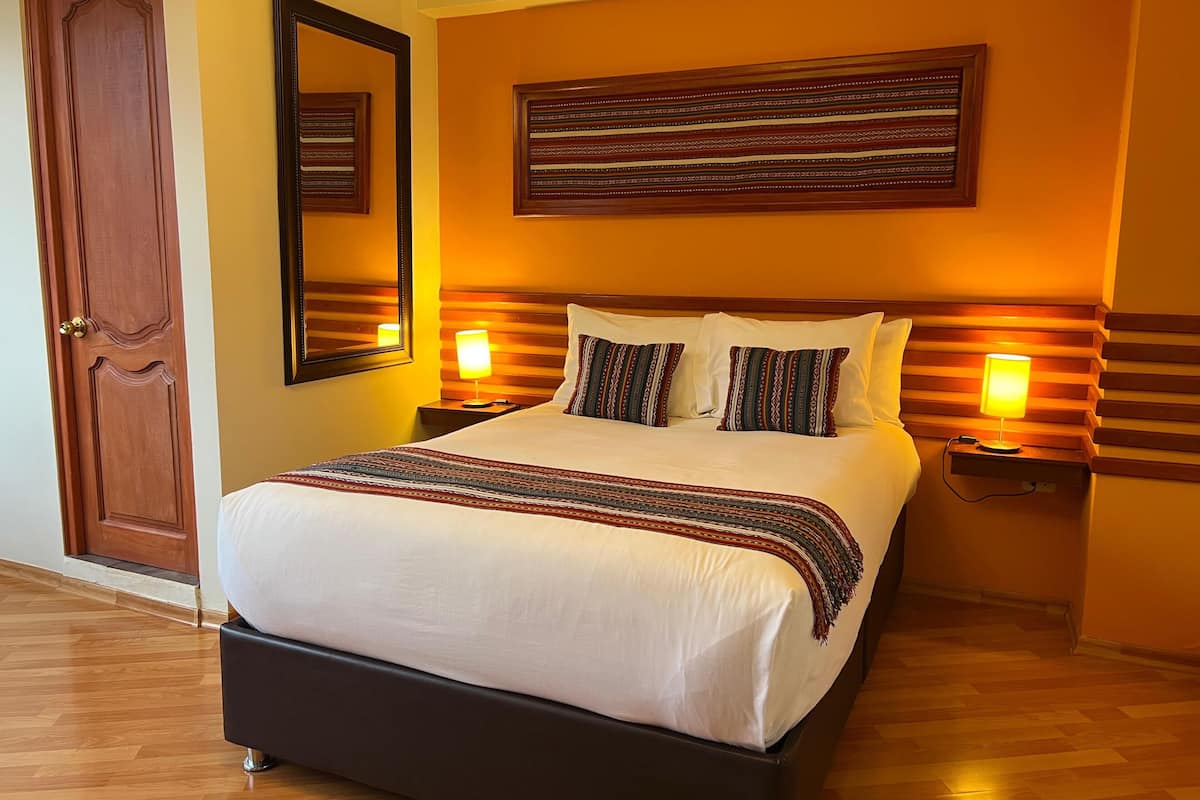 A hotel room with a large bed, two bedside lamps, a mirror, and a wooden door.