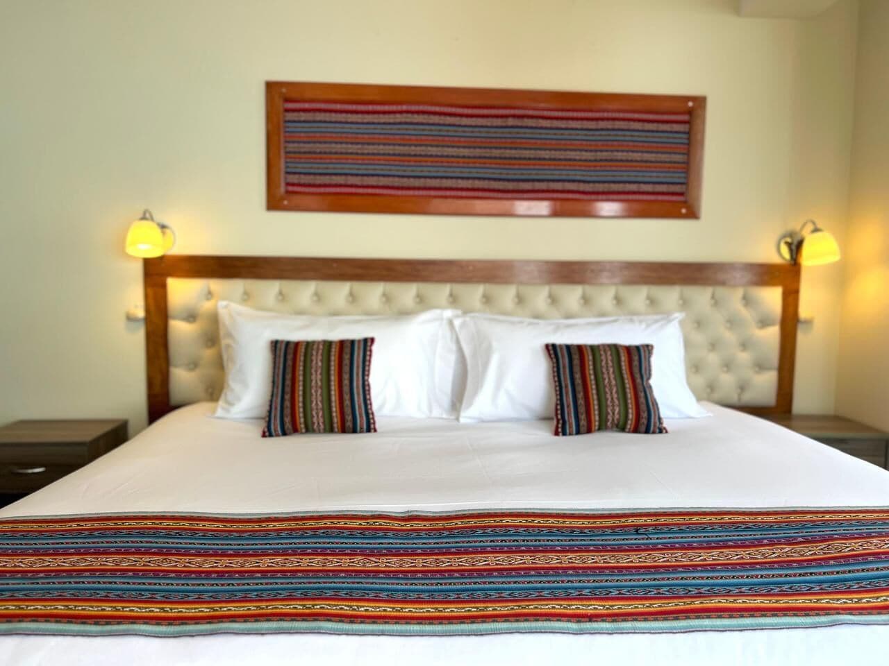 A bed with a tufted headboard, white bedding, and two pillows with striped patterns.