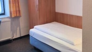 Ein kleines, gemütliches Zimmer mit einem Einzelbett, einem Holzschrank und einer Heizung.