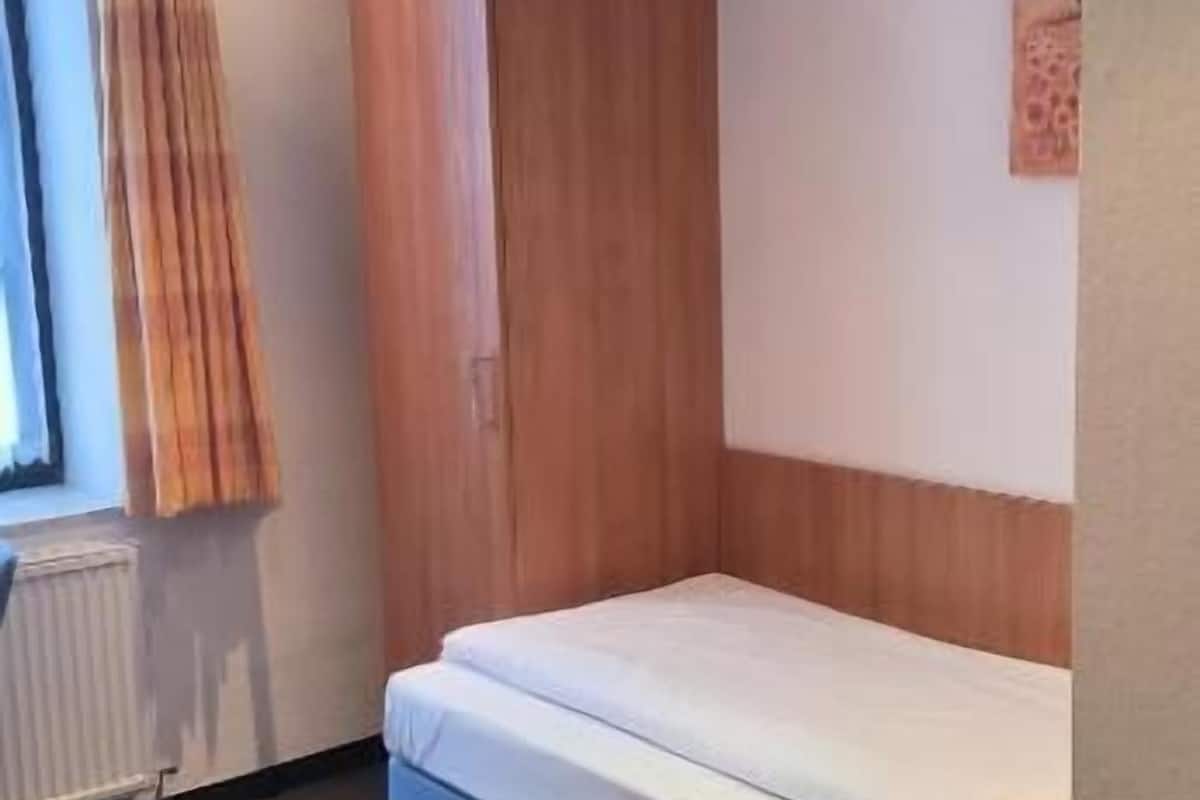 Une petite pièce, de taille modeste, comprenant un lit simple, une armoire en bois et un radiateur.