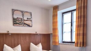 Ein Hotelzimmer mit zwei Betten, einem hölzernen Kopfteil, einem Bild an der Wand und einem Fenster mit Vorhängen.
