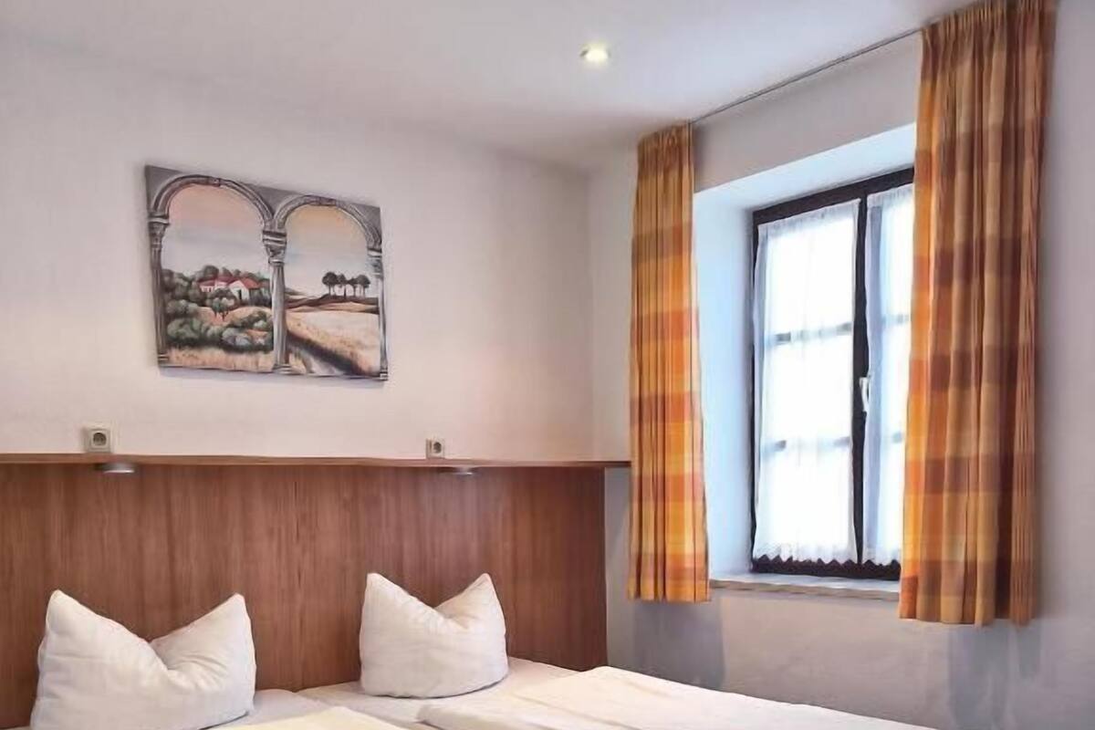 Une chambre d’hôtel avec deux lits, une tête de lit en bois, un tableau au mur et une fenêtre avec des rideaux.