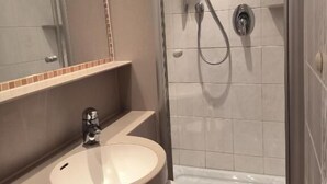 Ein modernes Badezimmer mit einer gläsernen Duschkabine, einem Waschbecken mit Spiegel darüber und einem Handtuch an der Wand.