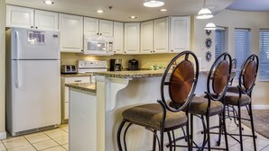 A kitchen with white cabinets, a refrigerator, a microwave, a coffee maker, and a bar area with chairs. - Golf Course Views • Fireplace • Free DOLLYwood Ticket • Near Dollywood (Pigeon Forge)