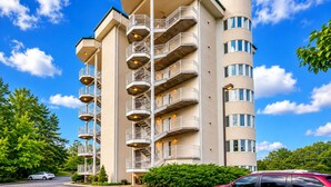 A multi-story residential building with balconies, a curved corner design, and a clear blue sky. - Golf Course Views • Fireplace • Free DOLLYwood Ticket • Near Dollywood (Pigeon Forge)