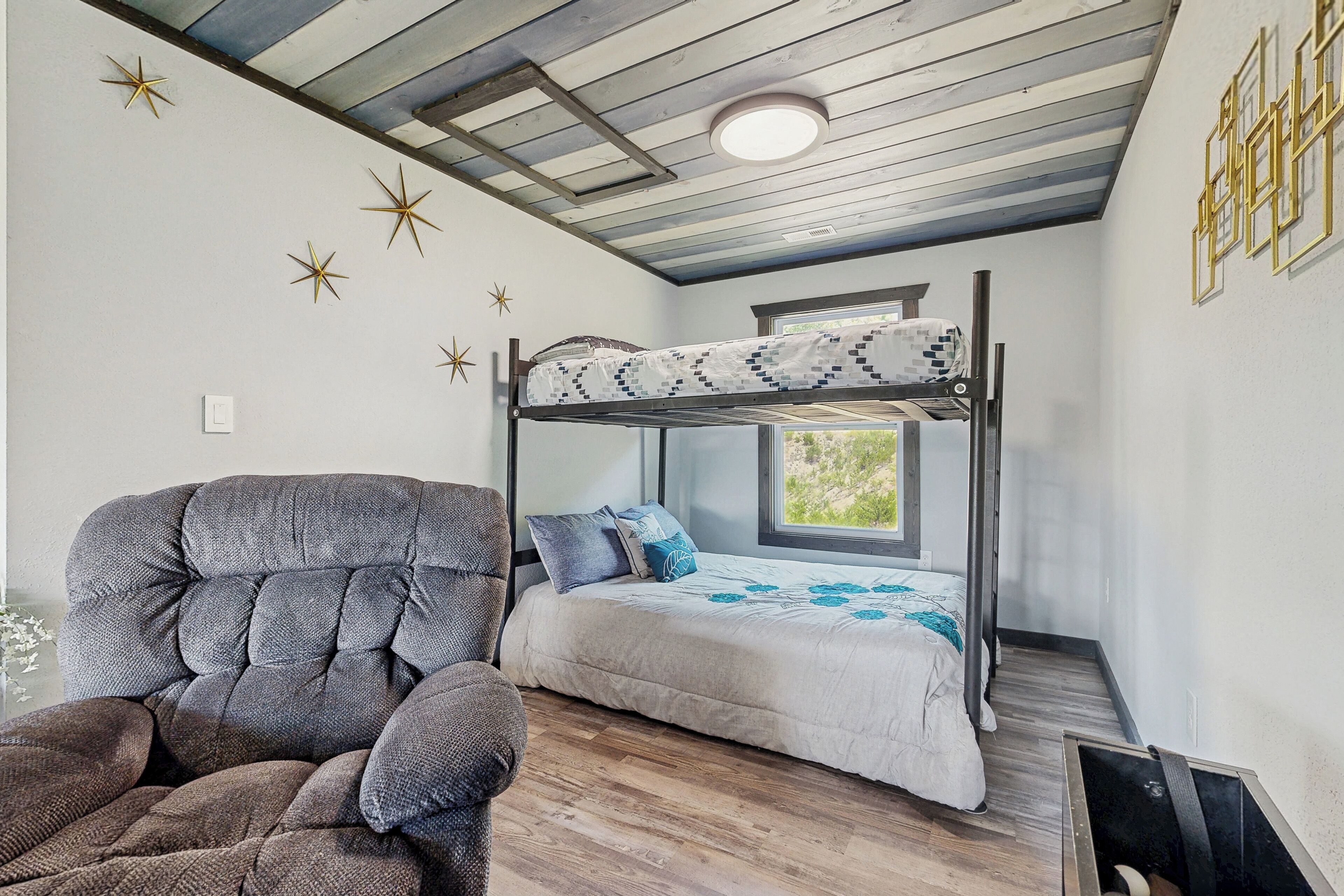 Un letto a castello con una coperta a motivi, una poltrona grigia imbottita e decorazioni a forma di stelle alle pareti.