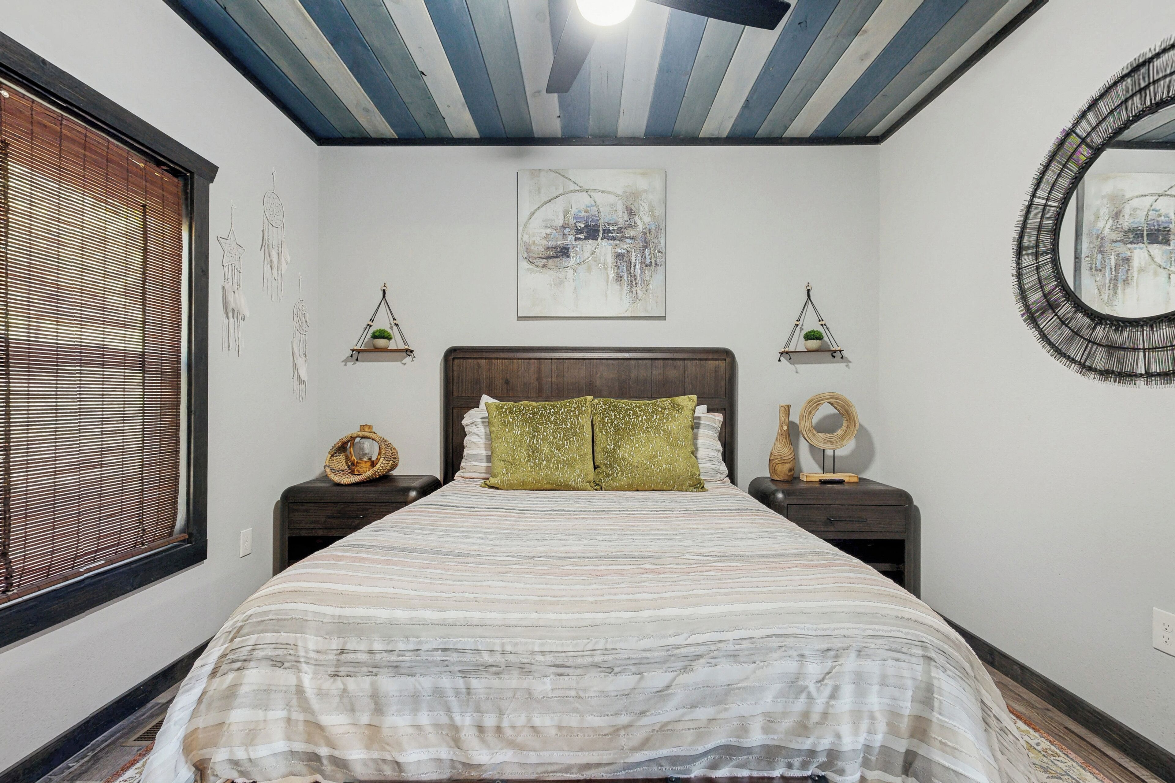 A bedroom with a bed, two nightstands, a ceiling fan, a window with blinds, and wall art.