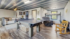 Una habitación amplia con una mesa de ping pong, un sofá, una mecedora y un ventilador de techo.