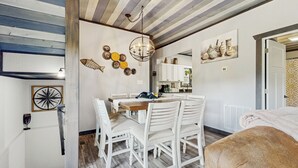 Un comedor con una mesa de madera y sillas blancas, una araña y detalles decorativos en la pared.