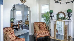 A spacious living room with a fireplace, a dining area with a chandelier, and a hallway leading to another room. - 4 BR Home w/ Modern Comforts & Park View (Savannah)