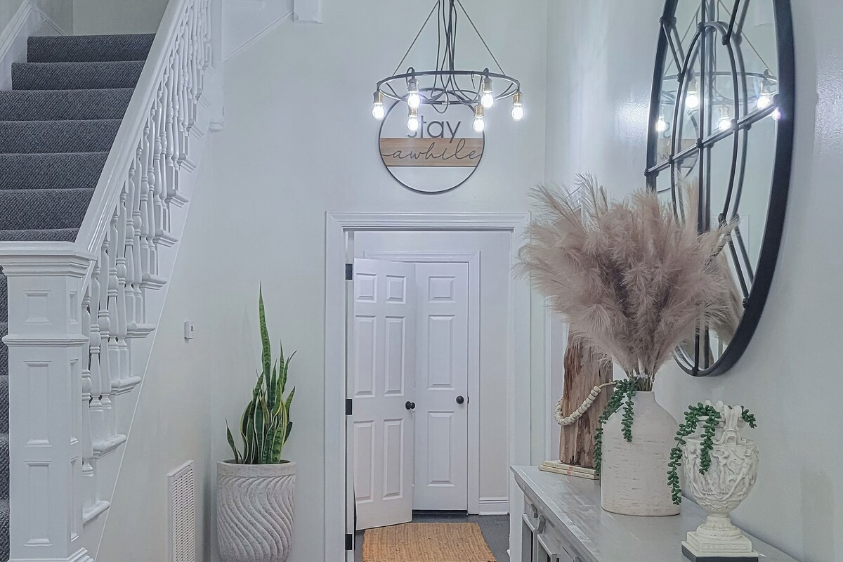 A staircase with white balusters, a white door, a wall-mounted sign with lights, and a mirror with a black frame.