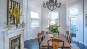 A dining room with a fireplace, chandelier, and large windows. - 4 BR Home w/ Modern Comforts & Park View (Savannah)