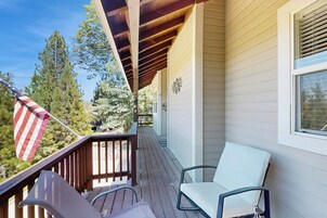 A wooden deck with a white chair and a metal chair, an American flag, and a window with blinds.