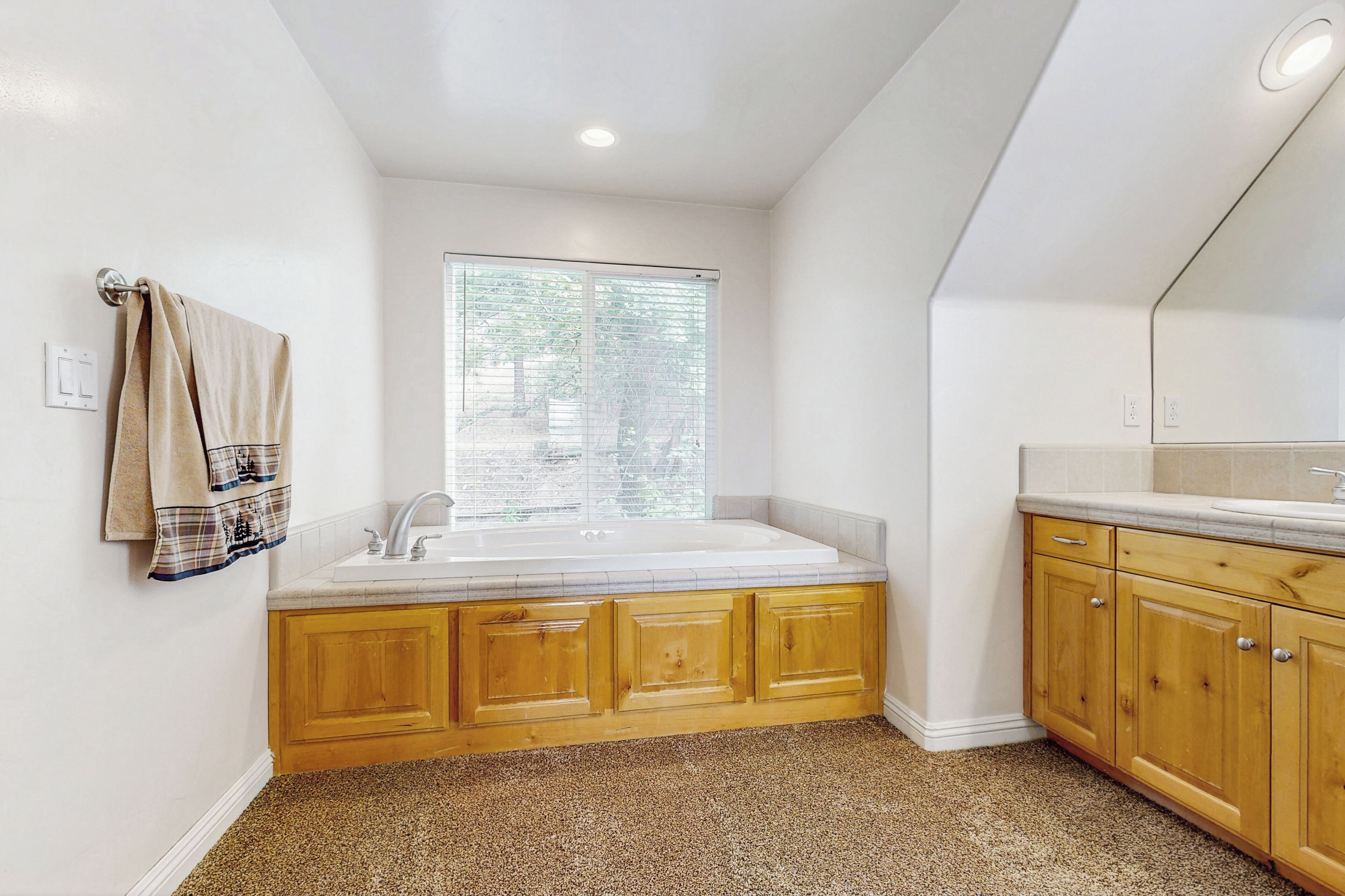 Un bagno con un lavandino bianco, mobili in legno, una finestra con persiane e un asciugamano beige appeso al muro.