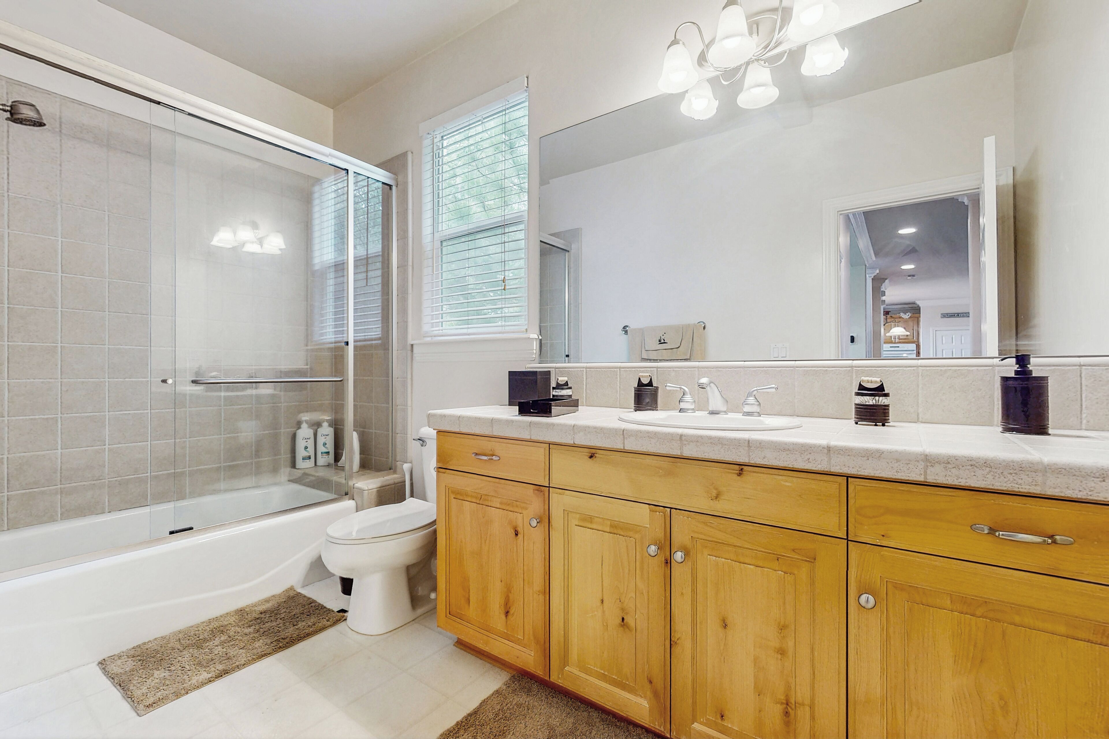 Un baño moderno con ducha de vidrio, inodoro, armarios de madera y un espejo grande.
