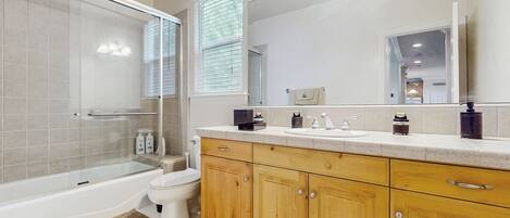 Un baño moderno con ducha de vidrio, inodoro, armarios de madera y un espejo grande.