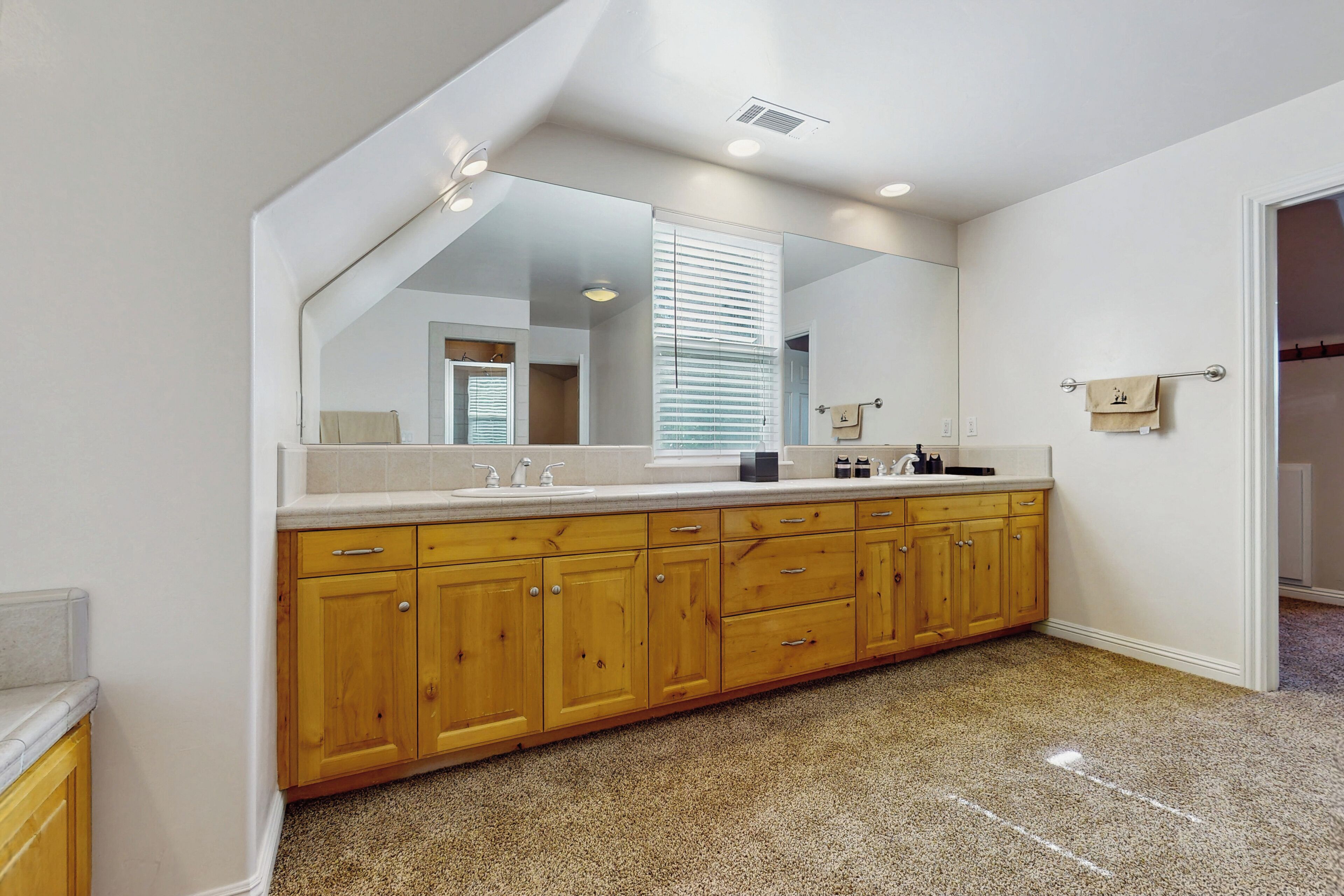 Un baño moderno con un espejo grande, armarios de madera y una alfombra color beige.