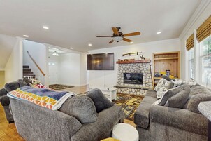 A living room with grey sofas, a stone fireplace, a flat-screen TV, and a ceiling fan.