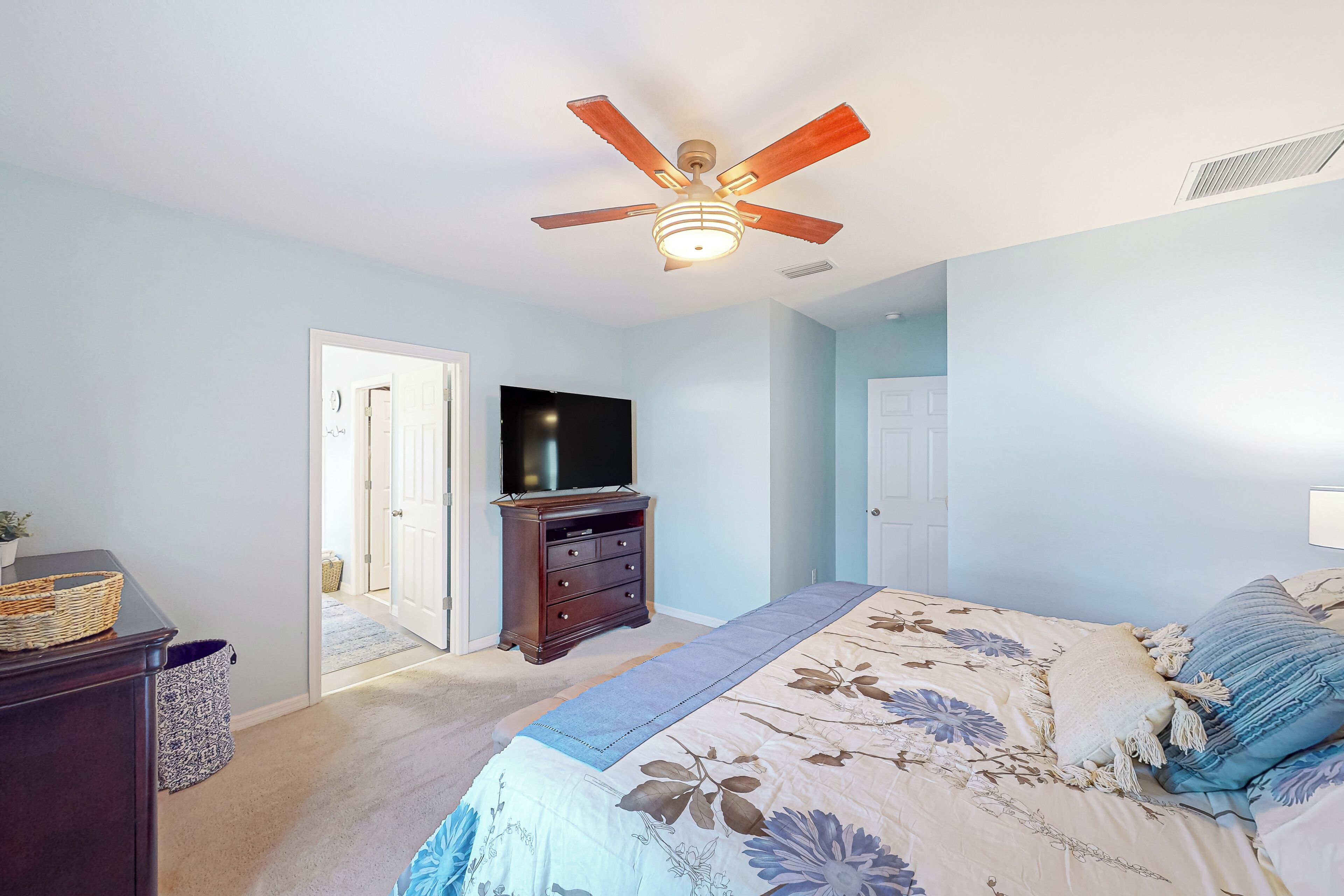 A bedroom with a bed, a ceiling fan, a dresser, a television, and a door leading to another room.