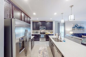 A modern kitchen with dark wood cabinets, stainless steel appliances, and a central island with a sink. - 3BR House w/ Enclosed Yard & Gas Grill (Groveland)