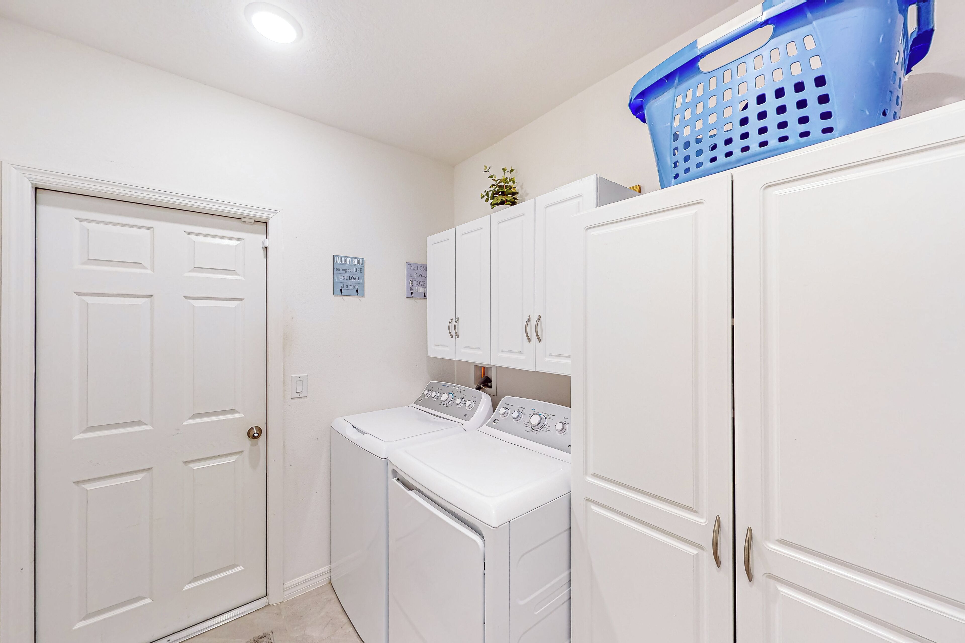 A laundry room with white cabinets, a washing machine, and a blue laundry basket on top.