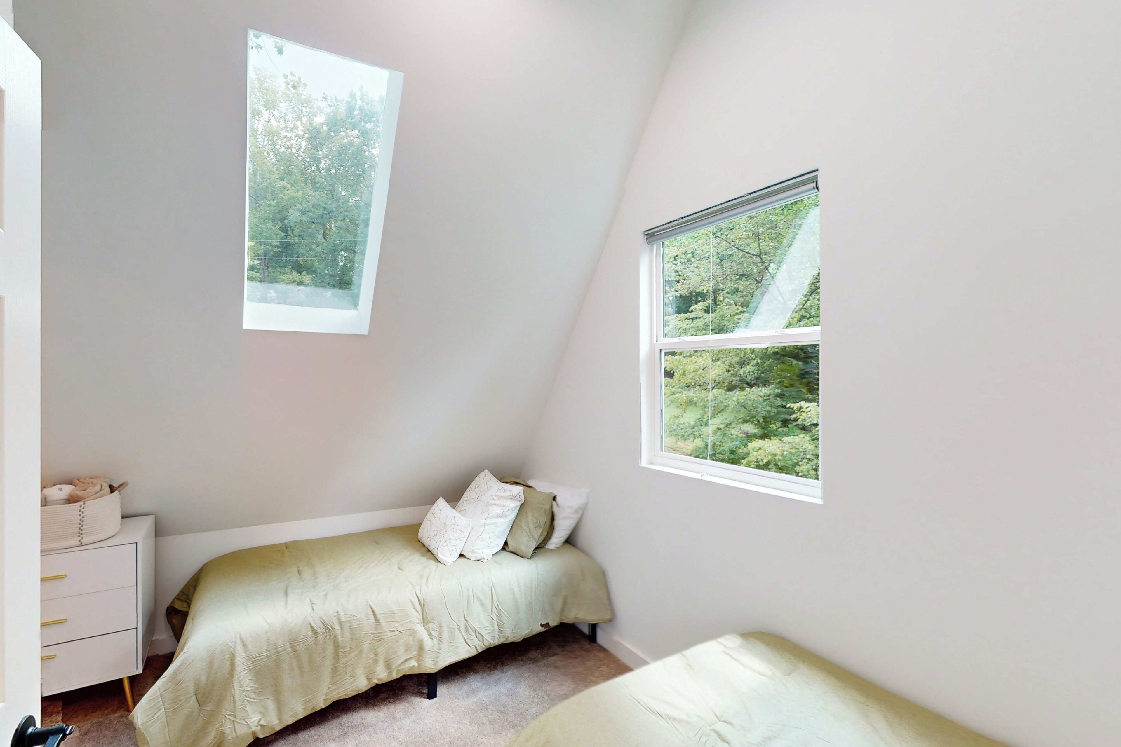 Un dormitorio con dos camas, una mesita de noche y dos ventanas que dan a zonas verdes.