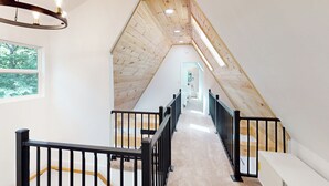 Eine enge, holzgetäfelte Treppe zum Dachboden mit schwarzen Geländern und einer Chandelier.