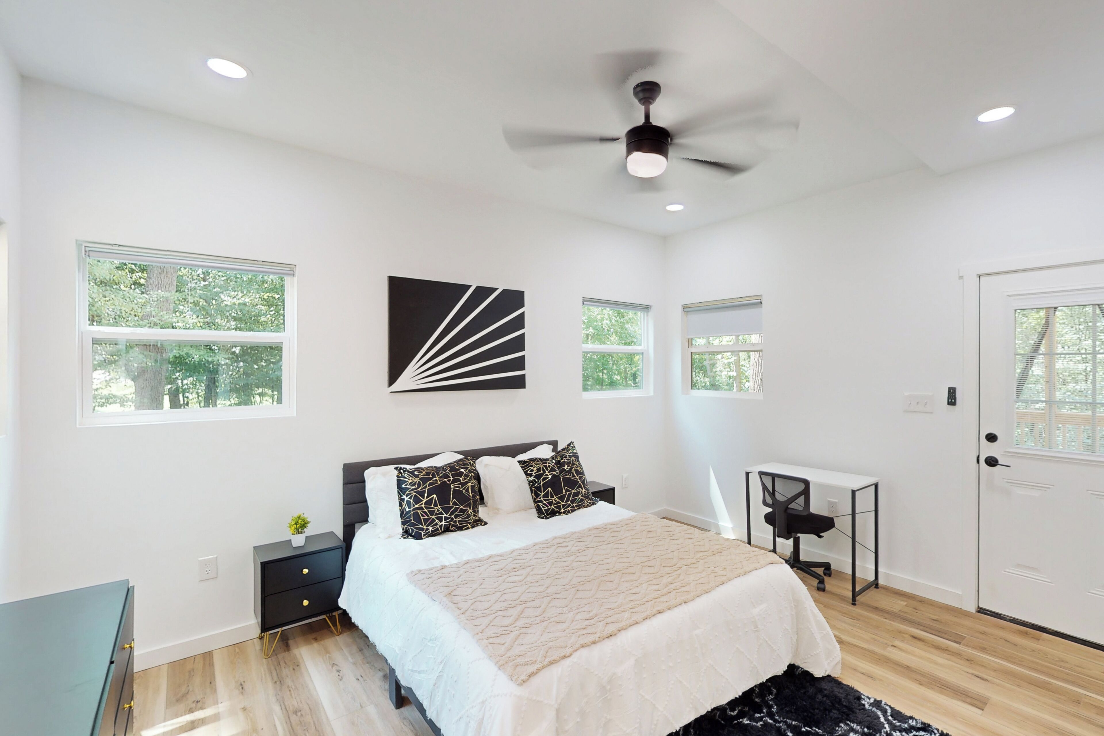 A modern bedroom with a bed, nightstands, a desk, and a ceiling fan.
